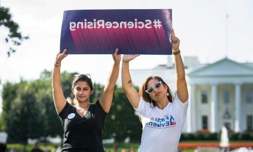 Two women holding a sign that says "Science Rising"